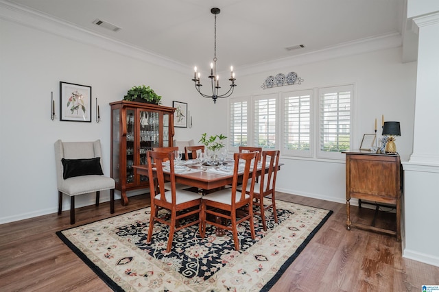 dining room featuring visible vents, wood finished floors, an inviting chandelier, and ornamental molding