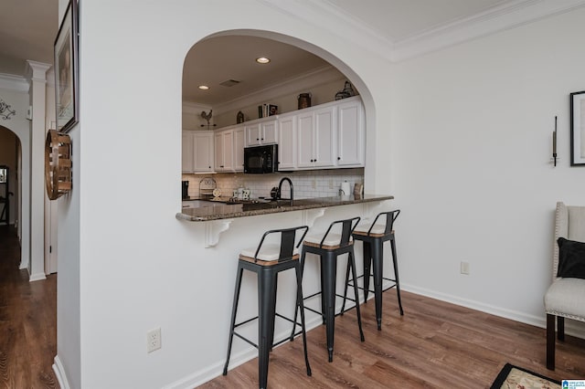 kitchen featuring arched walkways, backsplash, ornamental molding, and black microwave