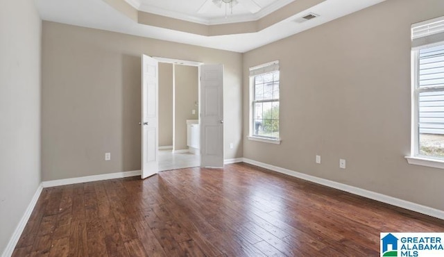 unfurnished bedroom with a tray ceiling, multiple windows, visible vents, and wood-type flooring