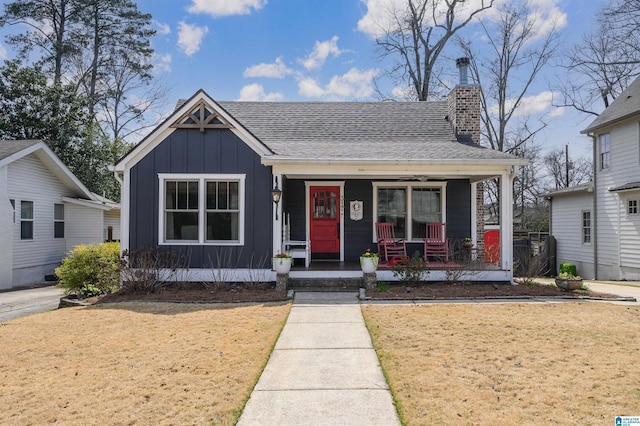 bungalow-style home with roof with shingles, a porch, a chimney, a front lawn, and board and batten siding