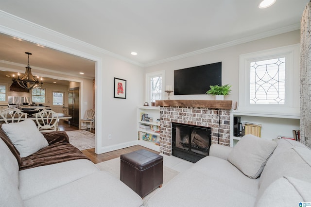 living room featuring wood finished floors, baseboards, ornamental molding, a brick fireplace, and a notable chandelier