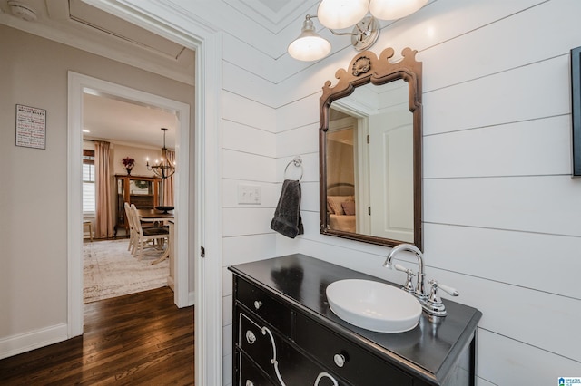 bathroom with baseboards, ornamental molding, wood finished floors, a notable chandelier, and vanity