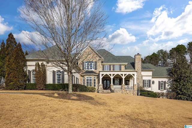 traditional home with stone siding, a chimney, covered porch, and a front yard