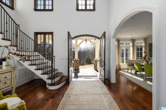 foyer with visible vents, arched walkways, wood-type flooring, and stairs