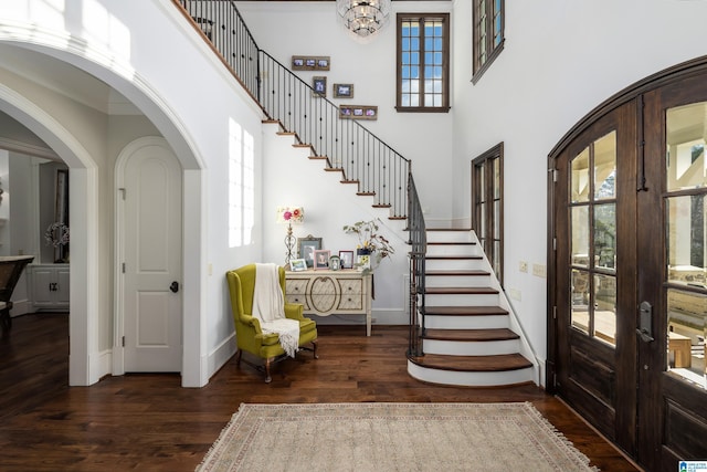 foyer featuring wood finished floors, french doors, arched walkways, baseboards, and a towering ceiling