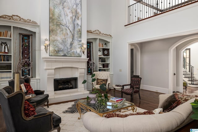 living area featuring a fireplace with raised hearth, wood finished floors, arched walkways, a high ceiling, and baseboards