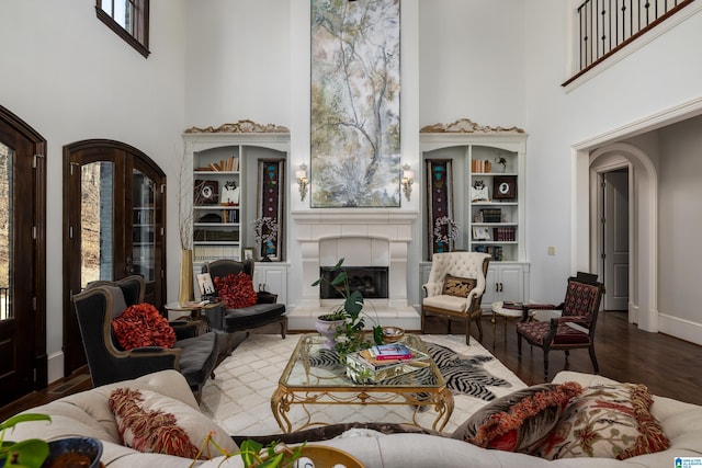 living area featuring arched walkways, a healthy amount of sunlight, wood finished floors, and a fireplace