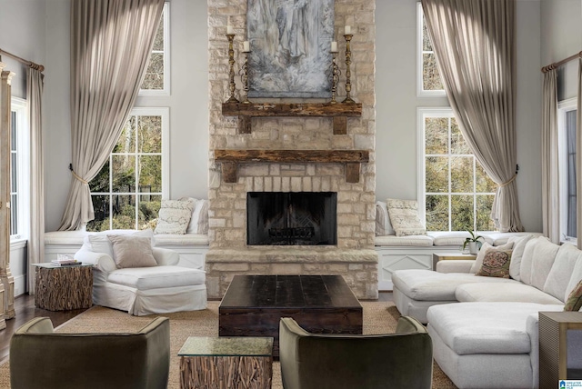 living room with a stone fireplace, a towering ceiling, and wood finished floors