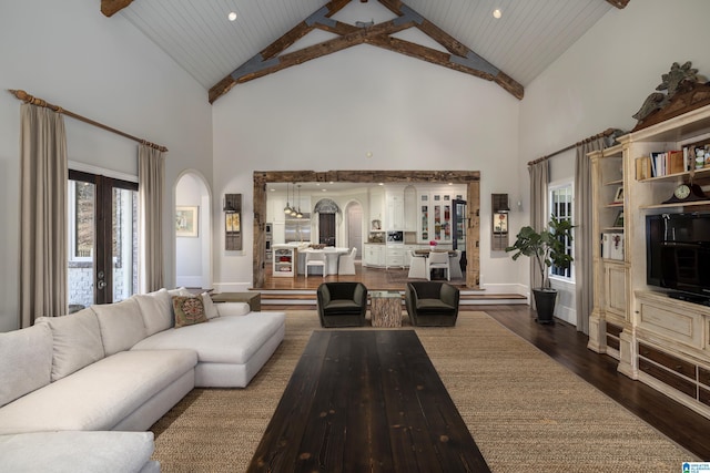 living room featuring arched walkways, dark wood finished floors, high vaulted ceiling, and baseboards