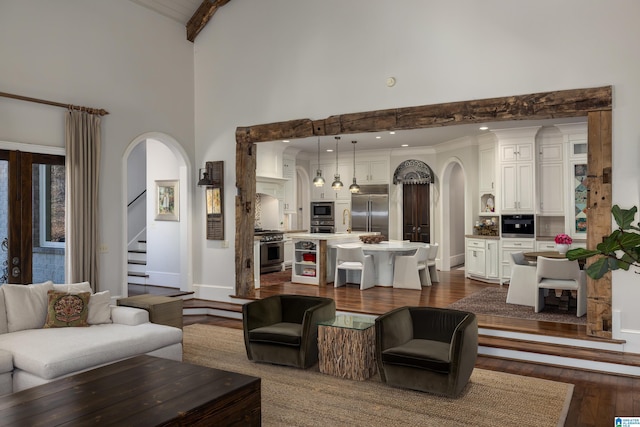 living area featuring stairway, dark wood finished floors, arched walkways, a towering ceiling, and beamed ceiling