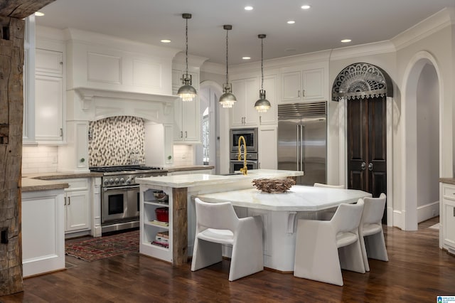 kitchen featuring built in appliances, backsplash, white cabinetry, and an island with sink