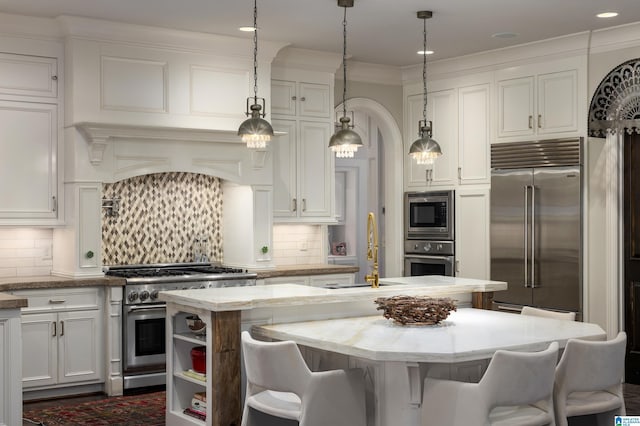 kitchen featuring built in appliances, backsplash, an island with sink, and a sink