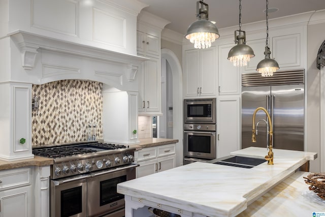 kitchen featuring white cabinetry, arched walkways, built in appliances, and a sink