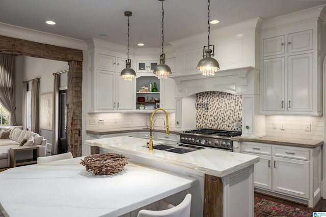 kitchen with white cabinets, stainless steel gas range, an island with sink, and a sink