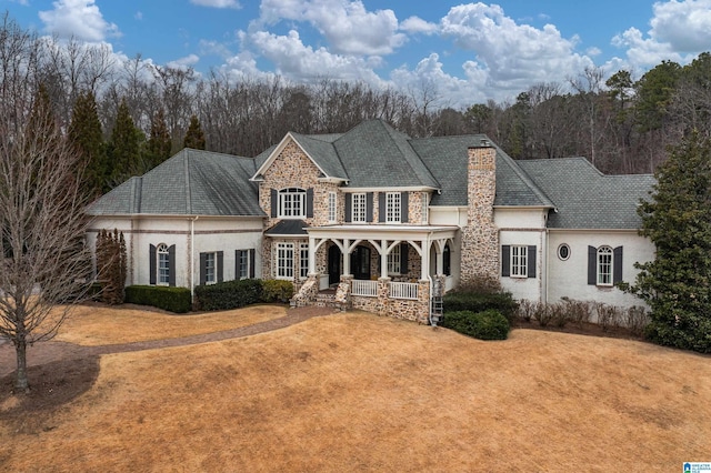 view of front of house with stucco siding, stone siding, a porch, a front yard, and a chimney