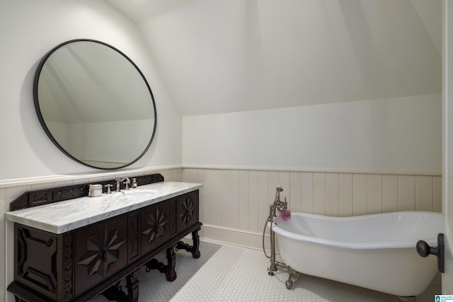 full bath with a wainscoted wall, a freestanding bath, vanity, and vaulted ceiling