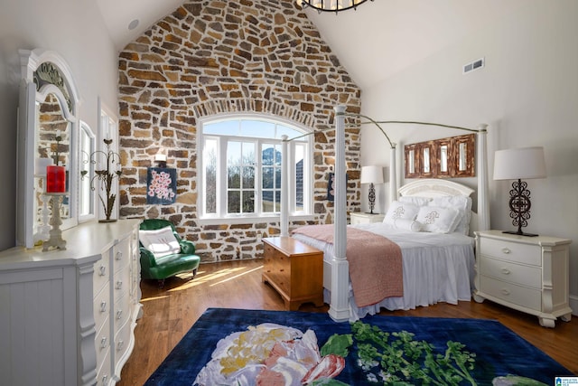 bedroom with visible vents, multiple windows, high vaulted ceiling, and wood finished floors