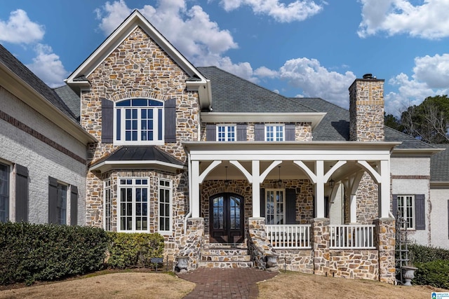 view of front of home with covered porch, french doors, stone siding, and a chimney