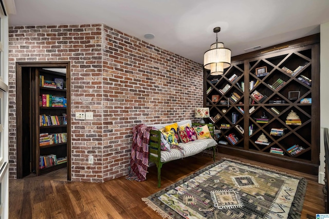 sitting room featuring visible vents, brick wall, and wood finished floors