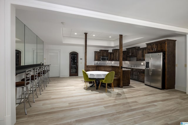 kitchen featuring a tray ceiling, stainless steel appliances, arched walkways, decorative backsplash, and dark brown cabinets