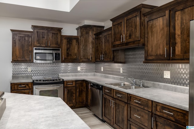 kitchen featuring dark brown cabinetry, light countertops, decorative backsplash, appliances with stainless steel finishes, and a sink