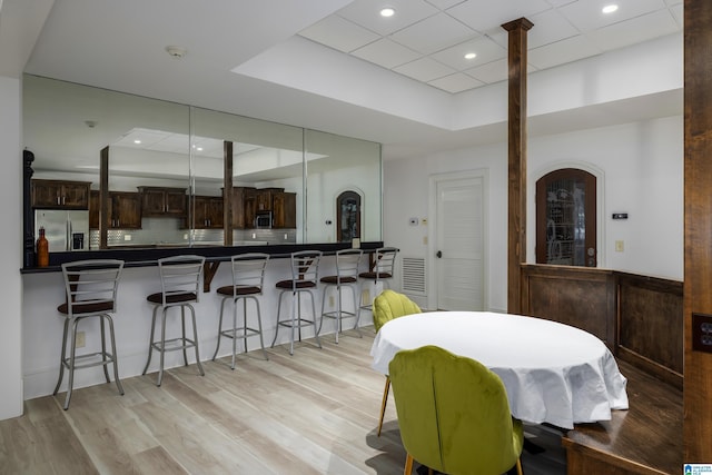 dining space featuring light wood-style flooring, recessed lighting, arched walkways, a raised ceiling, and ornate columns