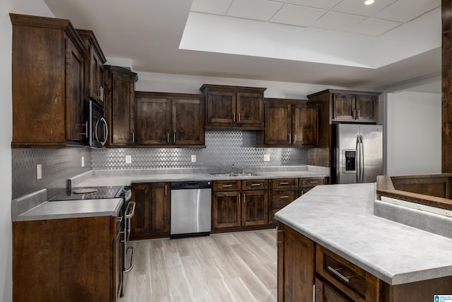 kitchen featuring a sink, stainless steel appliances, light wood-style floors, and backsplash