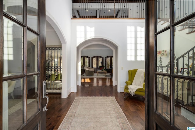 foyer entrance featuring dark wood finished floors, stairway, arched walkways, a high ceiling, and baseboards