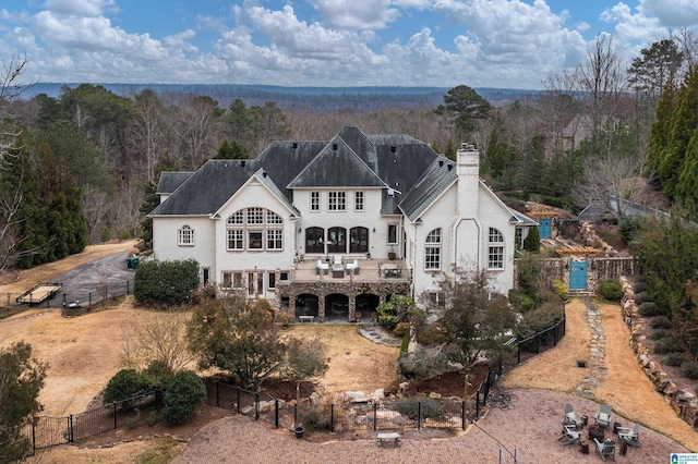 rear view of house featuring stucco siding, a forest view, fence private yard, a chimney, and a patio area