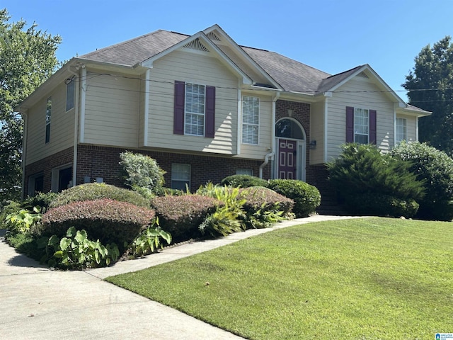 raised ranch featuring a front lawn, brick siding, and roof with shingles