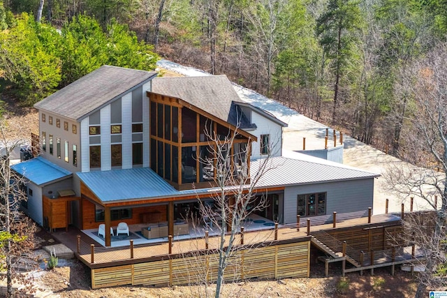 rear view of property featuring metal roof, a view of trees, a sunroom, and a wooden deck