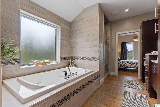 bathroom featuring a garden tub, wood finished floors, connected bathroom, a shower stall, and vaulted ceiling