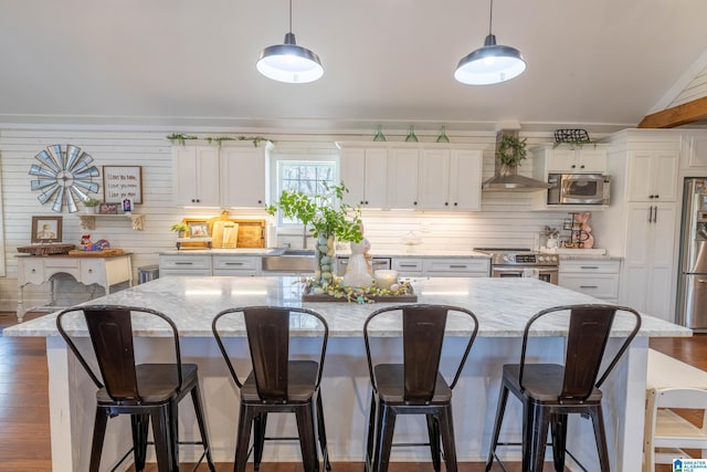 kitchen featuring a breakfast bar, a center island, appliances with stainless steel finishes, wall chimney exhaust hood, and white cabinets