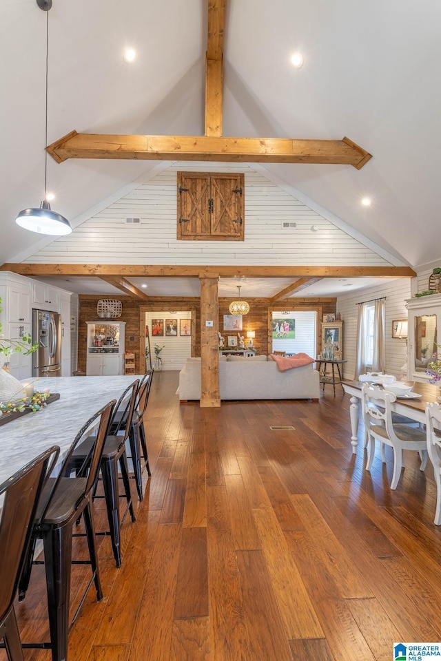 dining area featuring hardwood / wood-style floors, beamed ceiling, wood walls, and high vaulted ceiling