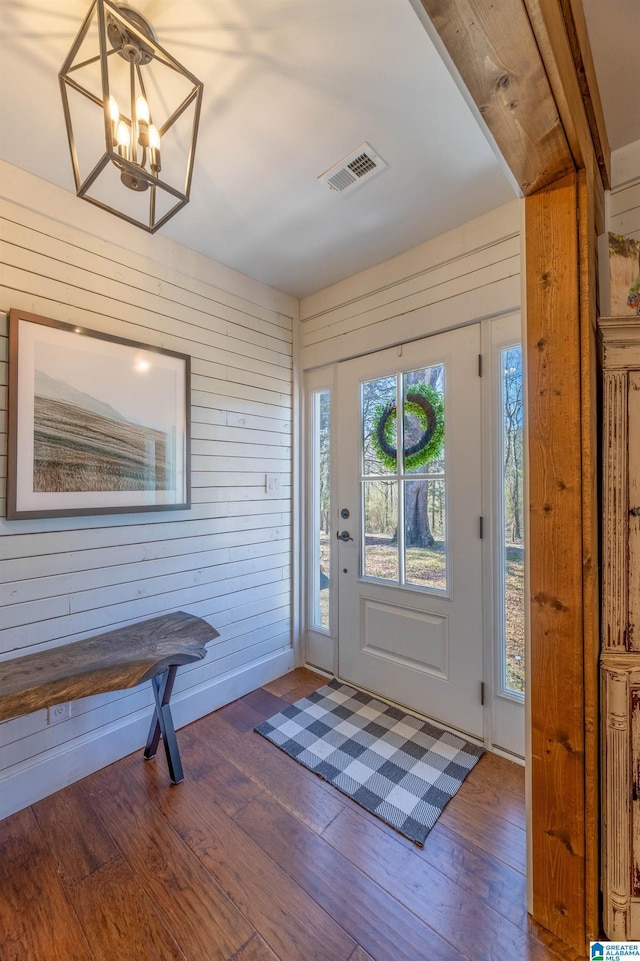 entryway with visible vents, wood-type flooring, wooden walls, and a chandelier