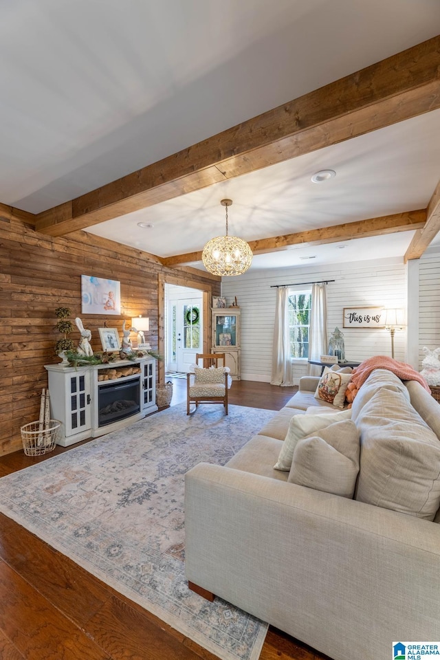 unfurnished living room with wooden walls, wood finished floors, an inviting chandelier, a fireplace, and beamed ceiling