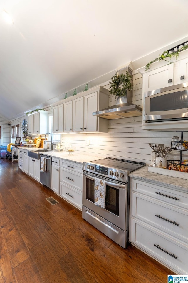 kitchen with lofted ceiling, white cabinets, stainless steel appliances, wall chimney exhaust hood, and dark wood-style flooring