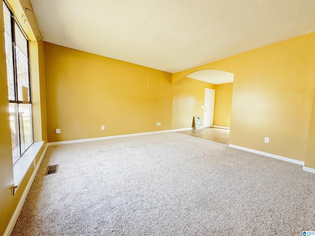 spare room with carpet, baseboards, visible vents, arched walkways, and a textured ceiling