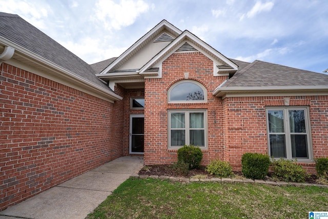 doorway to property with brick siding and roof with shingles