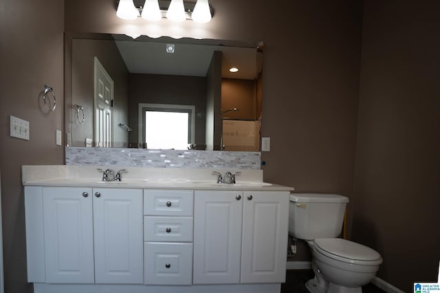 bathroom featuring tasteful backsplash, baseboards, toilet, double vanity, and a sink