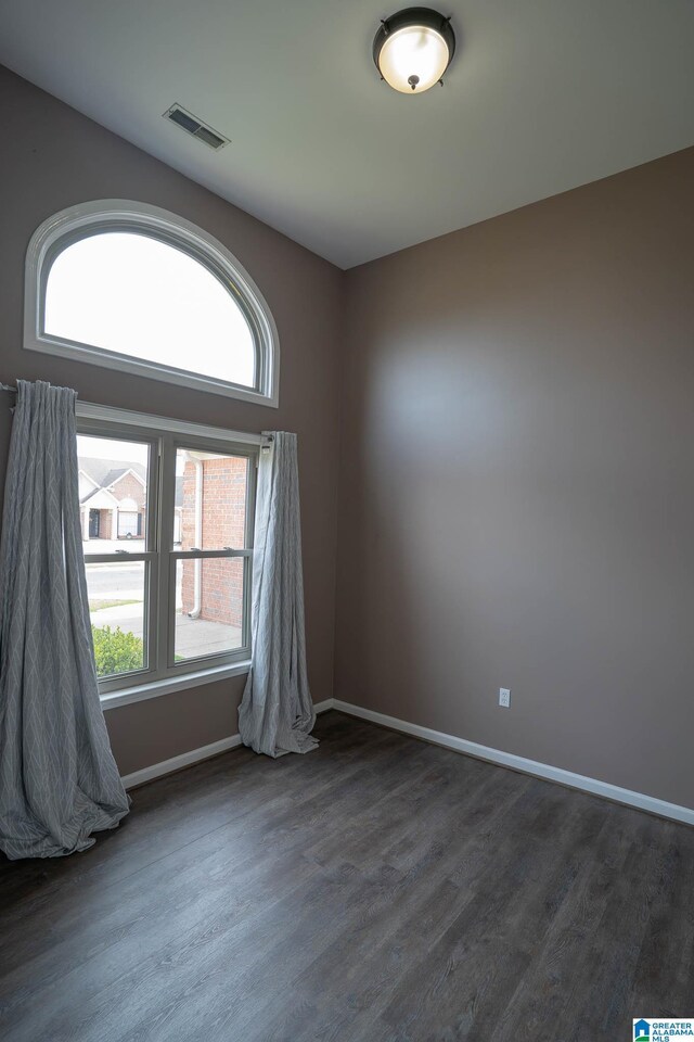 unfurnished room featuring visible vents, plenty of natural light, dark wood-type flooring, and baseboards