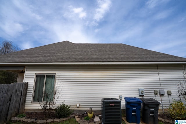 view of home's exterior featuring central AC unit, fence, and roof with shingles