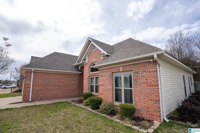 view of side of home with brick siding, a yard, and roof with shingles