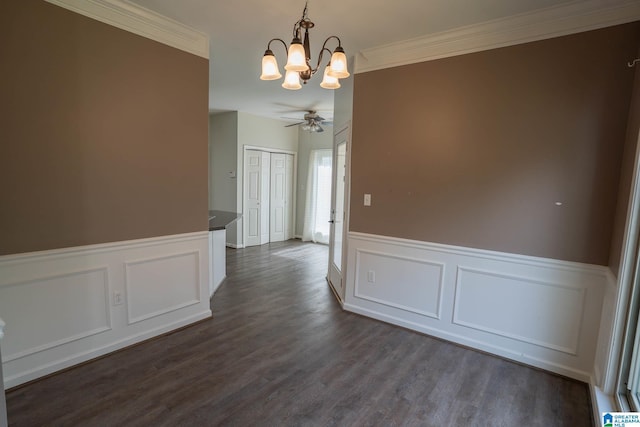 unfurnished dining area featuring dark wood finished floors, ceiling fan with notable chandelier, wainscoting, and ornamental molding