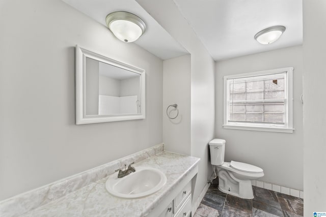 bathroom featuring stone tile floors, toilet, vanity, and baseboards