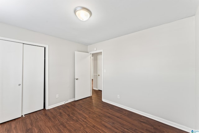 unfurnished bedroom featuring dark wood finished floors, a closet, and baseboards