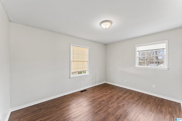 unfurnished room with visible vents, baseboards, dark wood-type flooring, and a healthy amount of sunlight