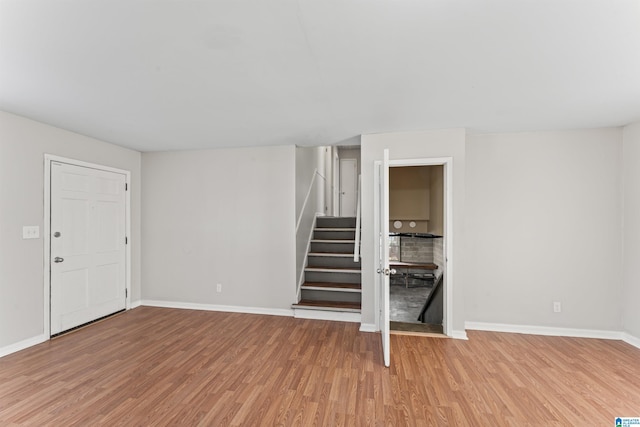 unfurnished living room featuring stairs, baseboards, and light wood finished floors