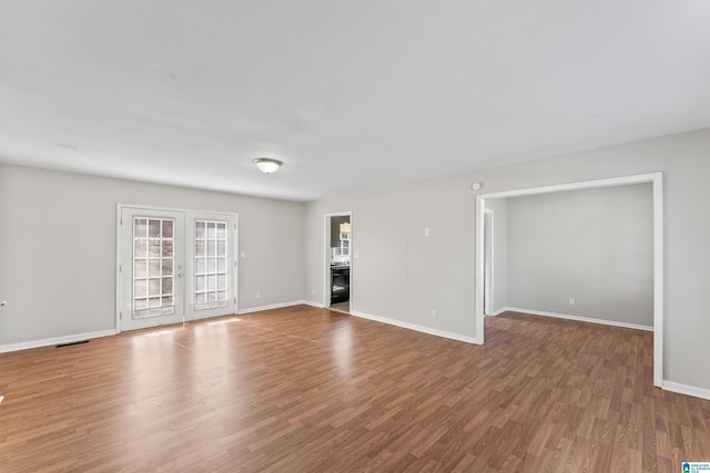 unfurnished living room featuring wood finished floors, baseboards, and french doors