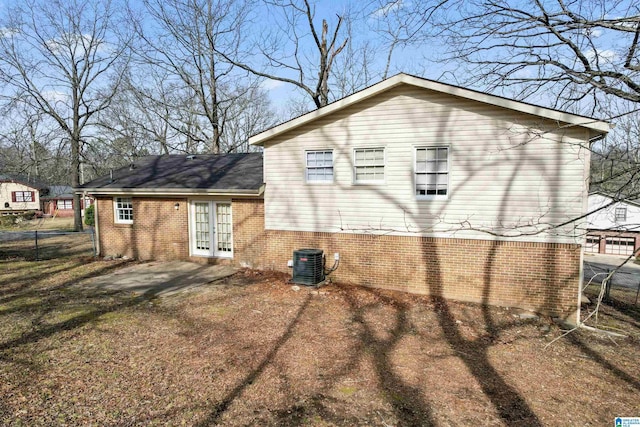 view of home's exterior featuring french doors, central air condition unit, brick siding, and fence